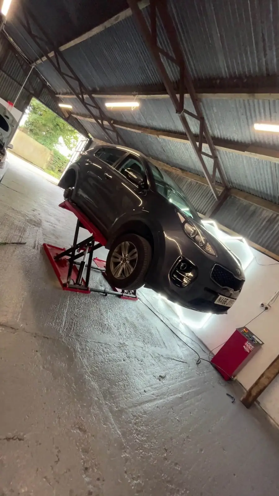 Grey Kia raised on a red scissor lift inside the unit
