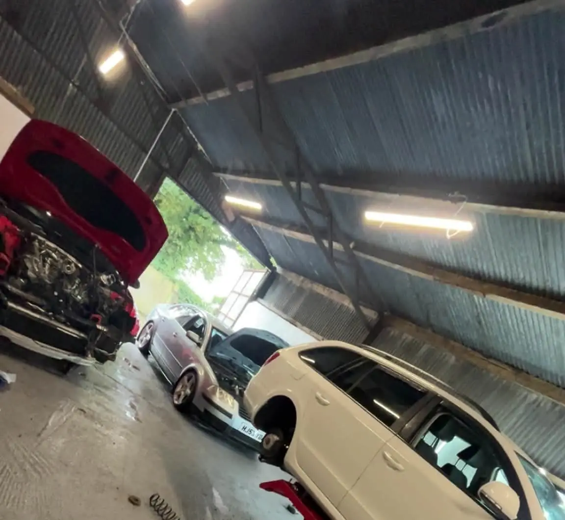 Three cars in the unit: a red car with its front end off, a silver Passat with the bonnet up and a white estate on the lift with a wheel off